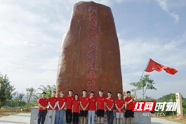 服务团队员在湖南省基层党建示范村标志前合影留念。